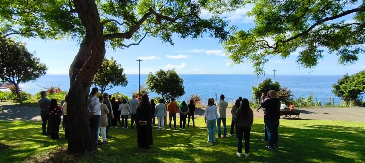 a group standing together under a tree by the ocean